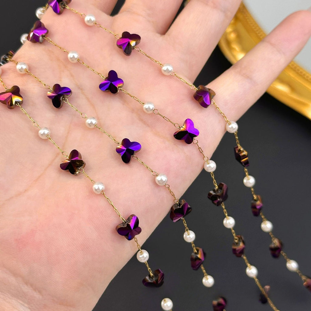 Hand holding gold chain strands with iridescent purple butterfly charms and white pearl beads