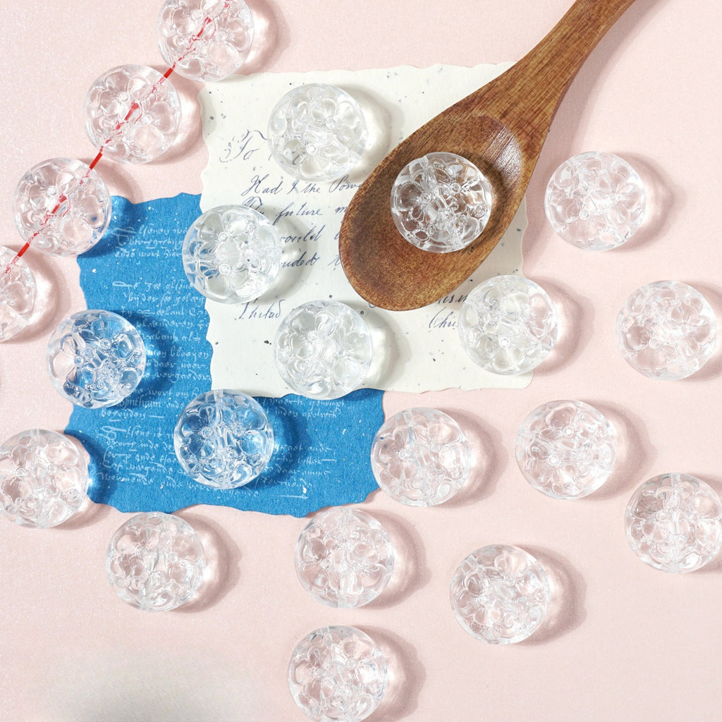 Clear round textured glass beads on pink with a wooden spoon and blue and white paper