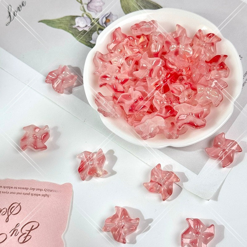 Pink translucent 20mm carved glass windmill beads in a small white dish with loose beads on a light surface