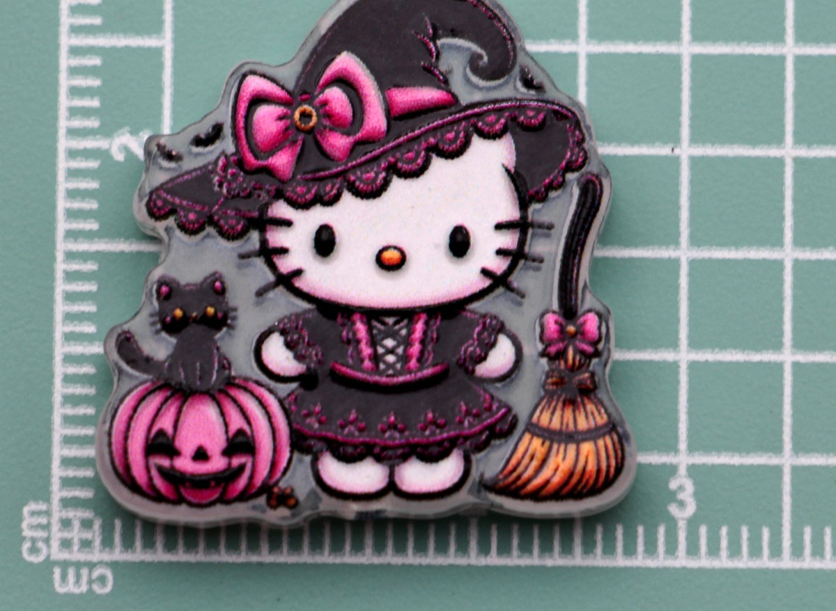 Hello Kitty black witch acrylic charm with pink bow, black cat, pink pumpkin, and broom on green cutting mat