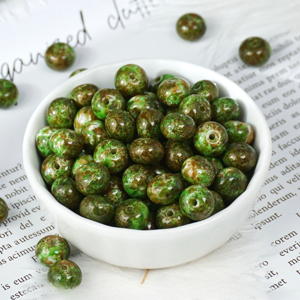 Green marbled beads with brown speckles in a small white porcelain bowl on a printed page background