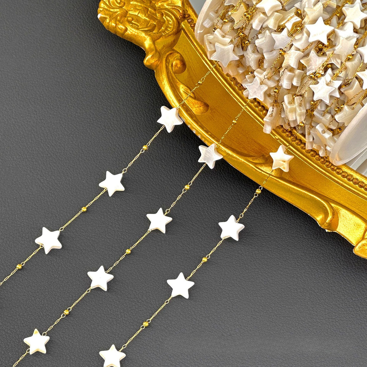 Strands of gold chain with white star beads draped over an ornate gold tray on a dark gray surface