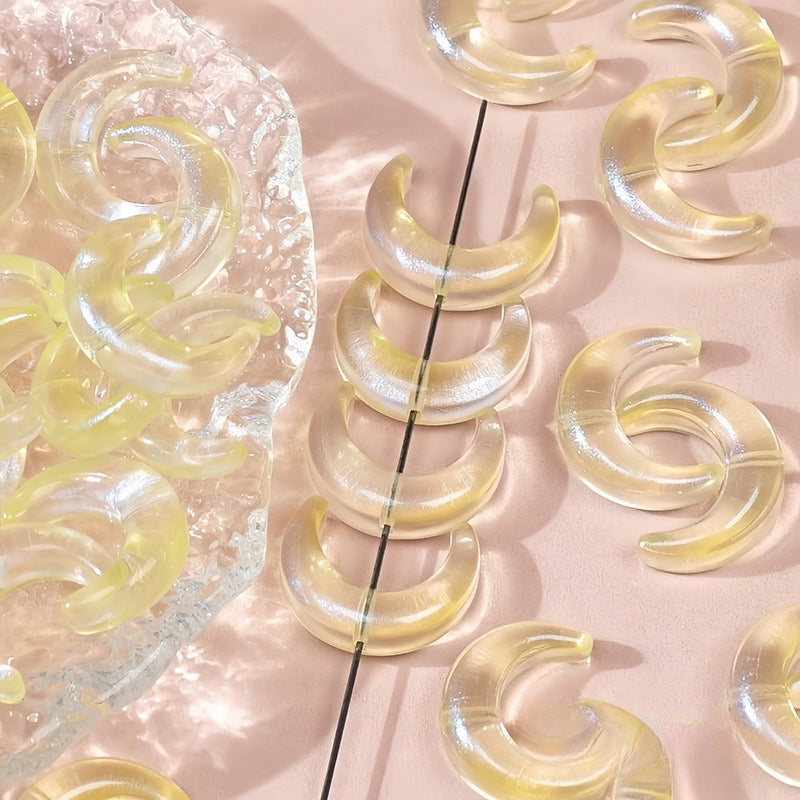 Translucent pale yellow glazed glass crescent moon beads, some strung on a black string and others on a pink surface