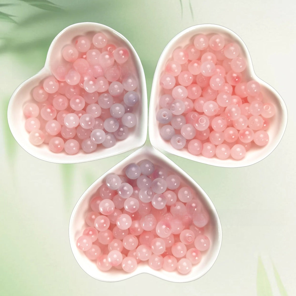 Three heart-shaped bowls of translucent pink beads on pale green