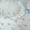 White translucent glass beads spilling from a glass bowl onto fabric