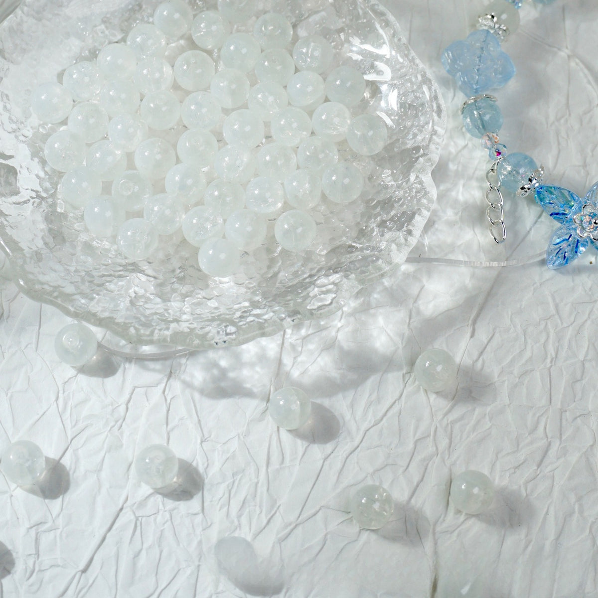 White translucent glass beads spilling from a glass bowl onto fabric