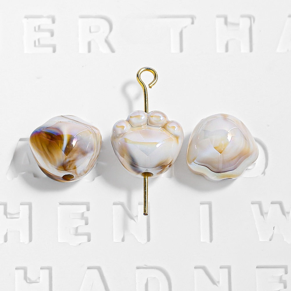 Three white and amber marbled paw-shaped beads, one on a gold eye pin