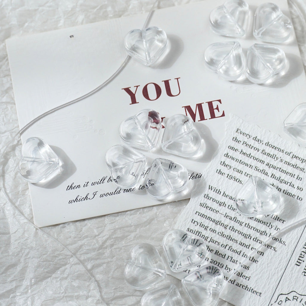 Clear glass heart-shaped and four-leaf clover beads arranged on a white textured surface with printed cards