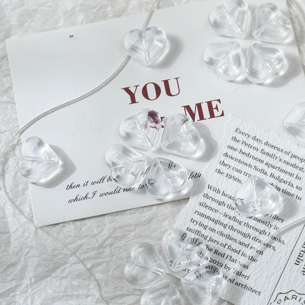 Clear glass heart-shaped and four-leaf clover beads arranged on a white textured surface with printed cards