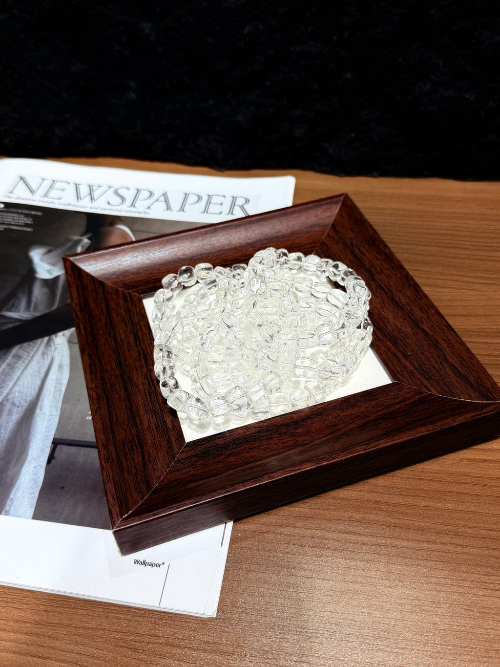 White quartz jelly-bean nugget bracelets coiled in a wooden tray on a table beside a newspaper
