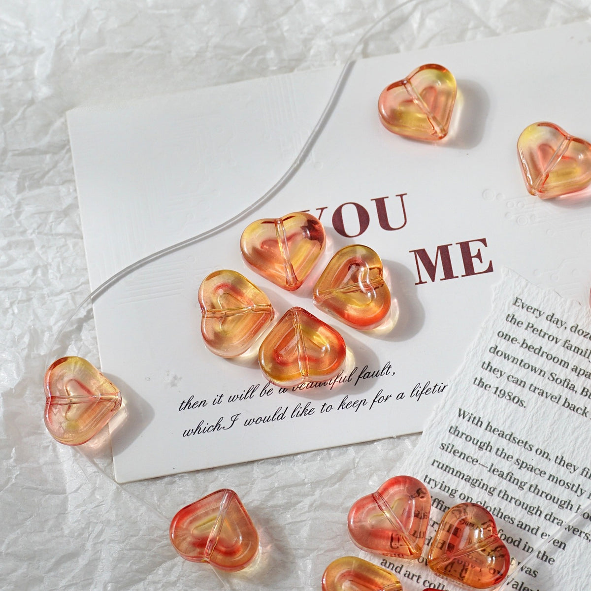 Heart-shaped translucent glass beads with orange and yellow gradients, arranged on a white card and printed paper