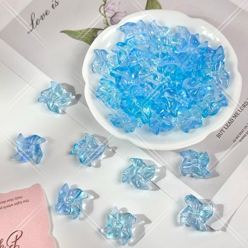 Light blue translucent 20mm carved glass windmill beads on a white surface with a white dish holding more beads