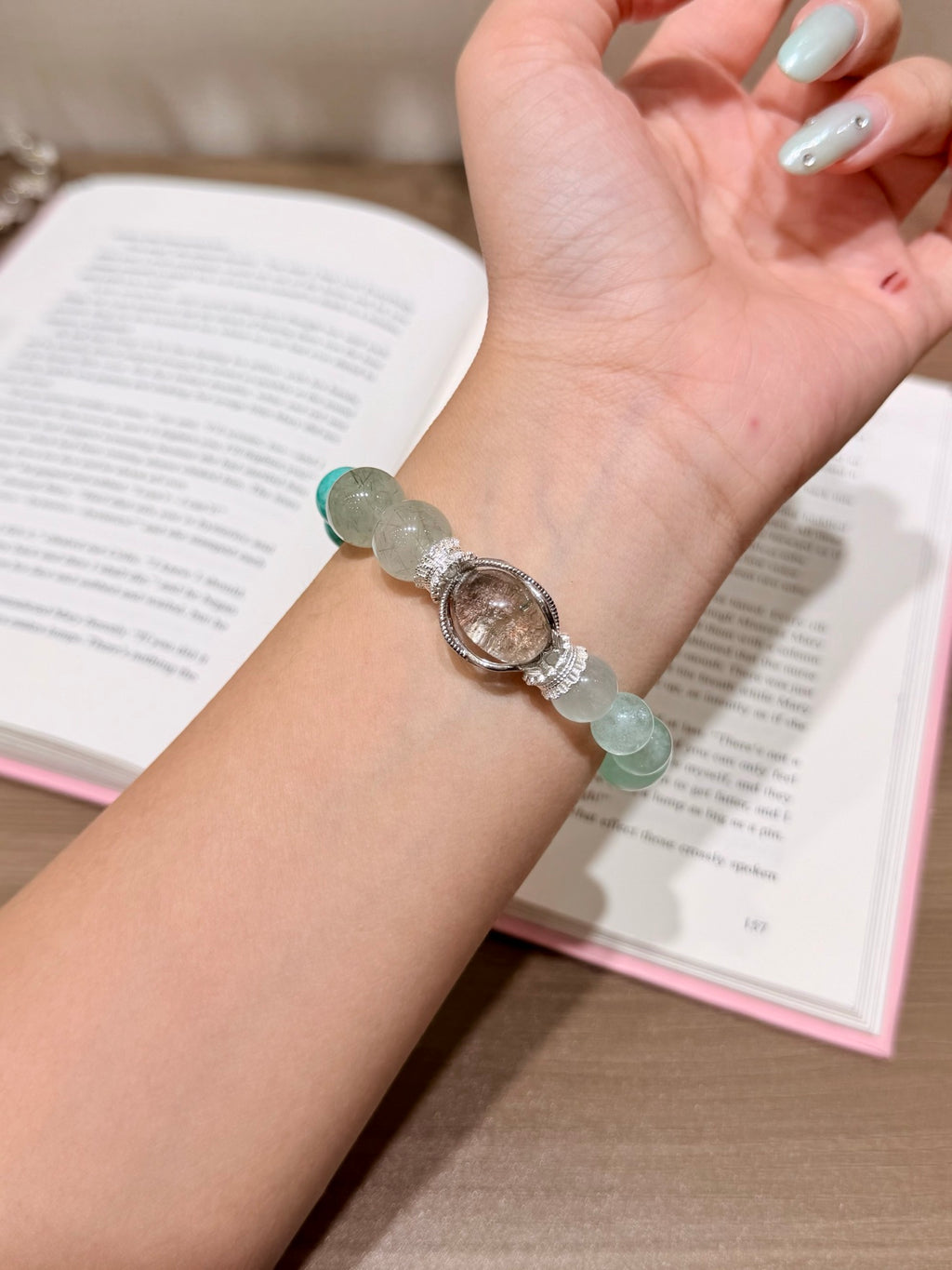 Hand holding forest mist bracelet with amazonite over open book