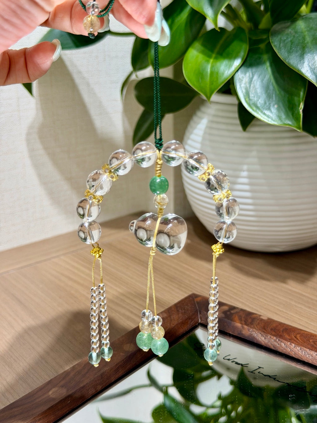 White crystal gourd car charm held against green plant
