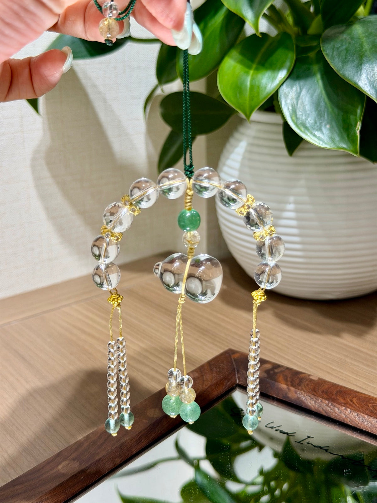 White crystal gourd car charm held against green plant