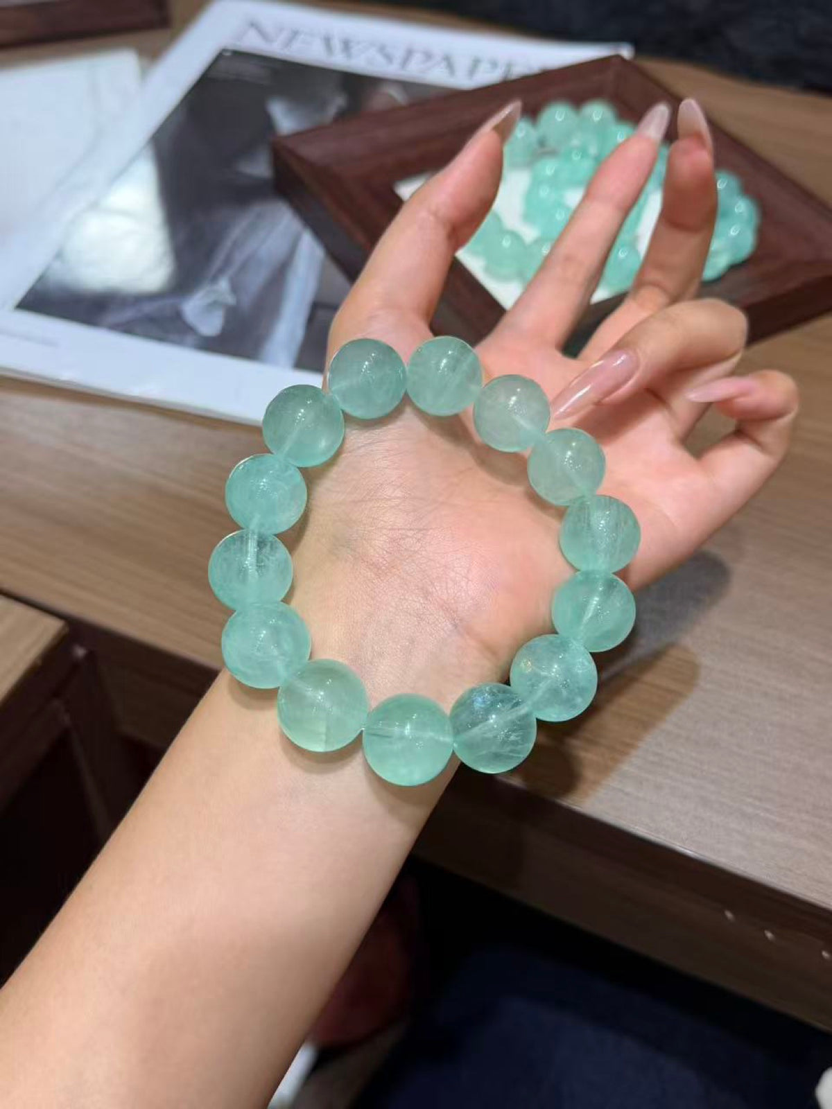 Hand displaying a mint green fluorite bracelet of large translucent round beads against a wooden table