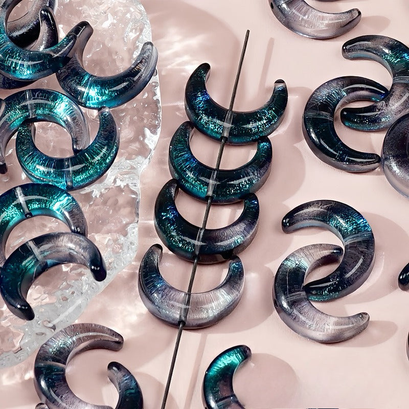 Teal and gray marbled glazed glass crescent moon beads, some strung on a wire and others on a clear ice block