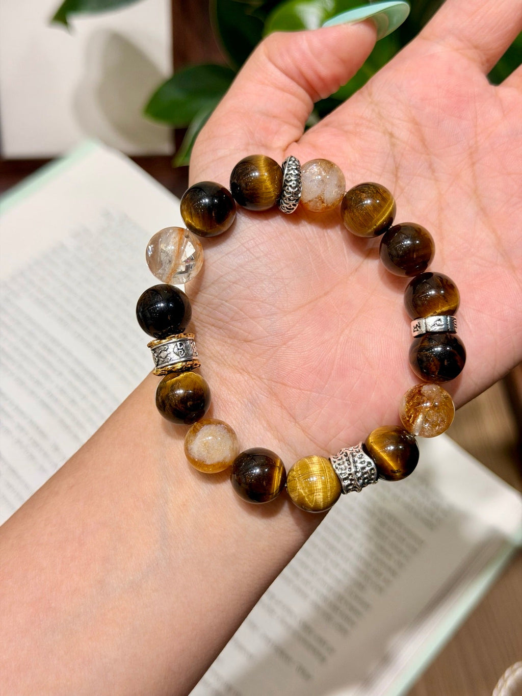 Tiger's eye and clear quartz bead bracelet with spacer beads held on an open palm over a book
