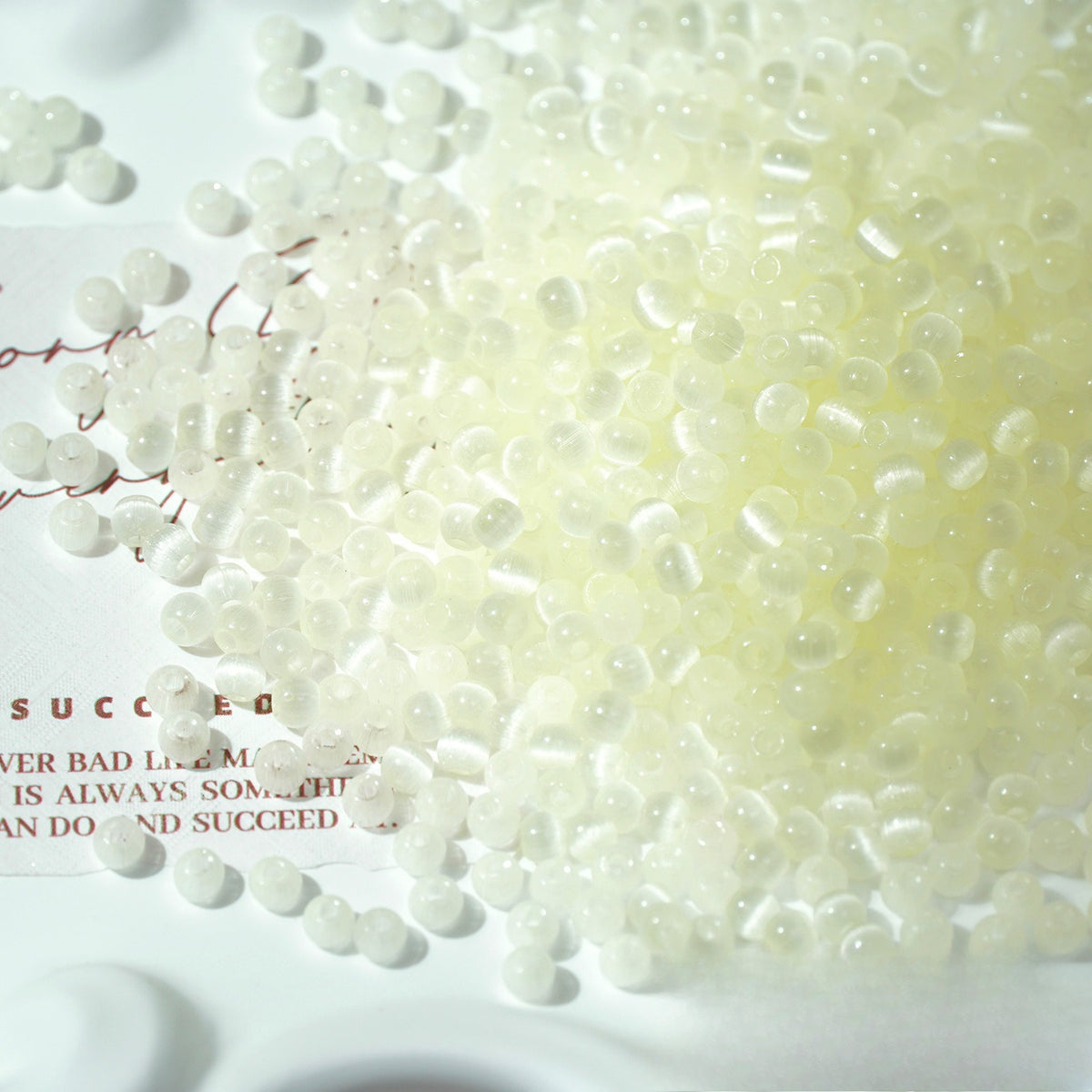 A close-up of translucent white plastic pellets or beads scattered across a white surface with printed text partially visible underneath.