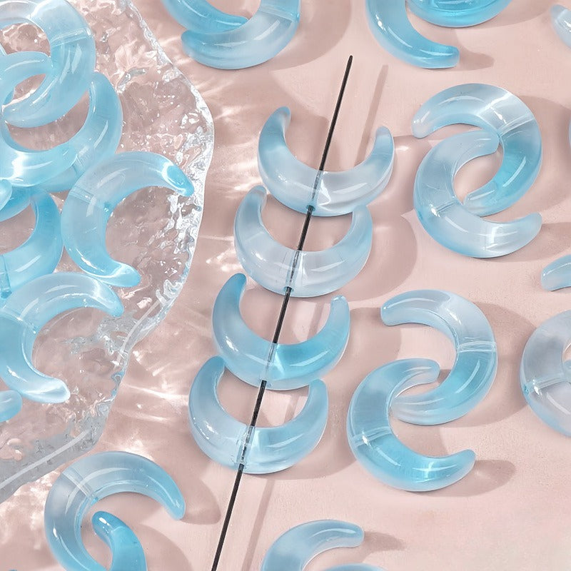 Light blue translucent glazed glass crescent moon beads, some strung on a black thread and others on a clear surface