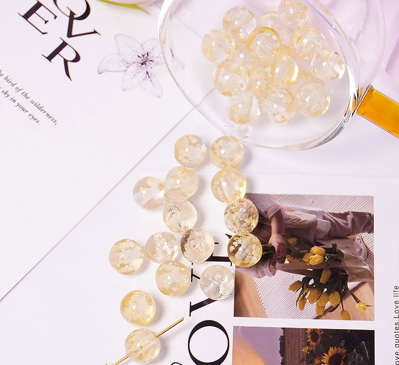 Golden yellow two-tone glow-in-the-dark glass beads spilling from a glass cup onto a printed card