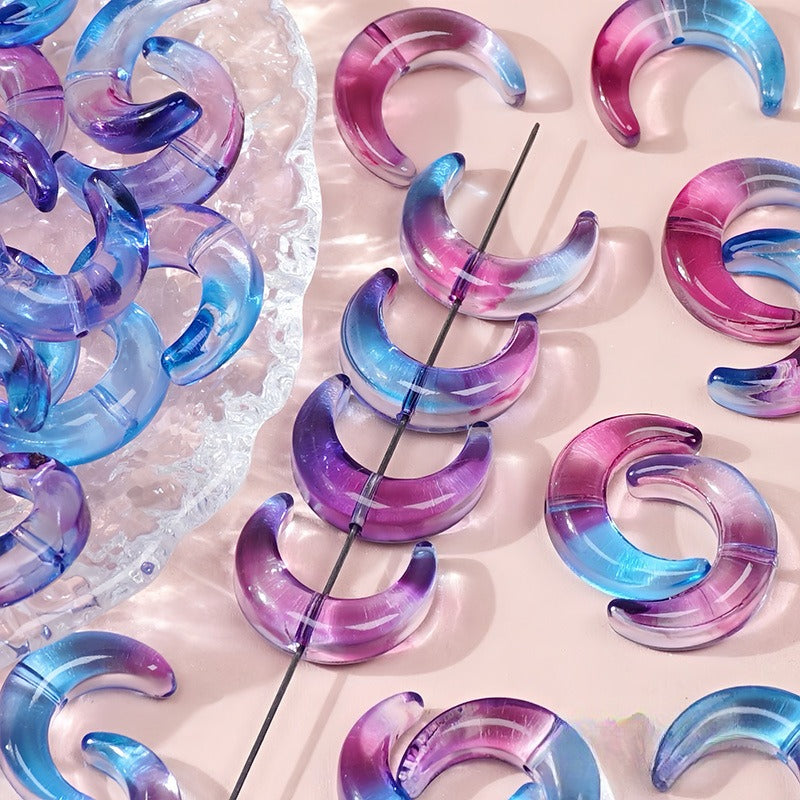 Blue purple and pink gradient glazed glass crescent moon beads, some threaded on a black string and others on a pink surface