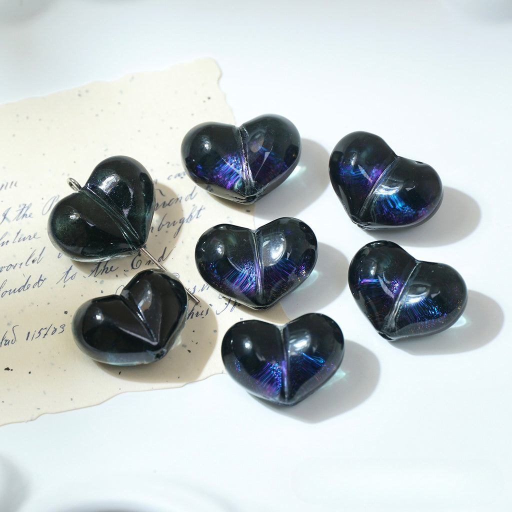 Seven glossy black heart-shaped glass beads with iridescent blue-purple sheen on white