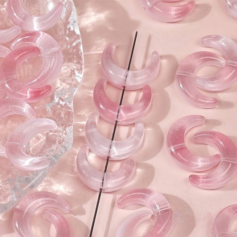 Pink translucent glazed glass crescent moon beads, some threaded on a black string and others on a pink surface