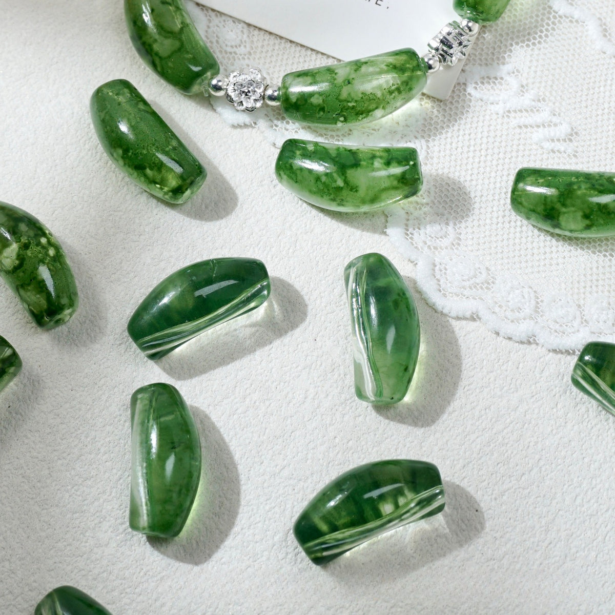 Green translucent glass beads with natural marbling, arranged on a white textured fabric background.