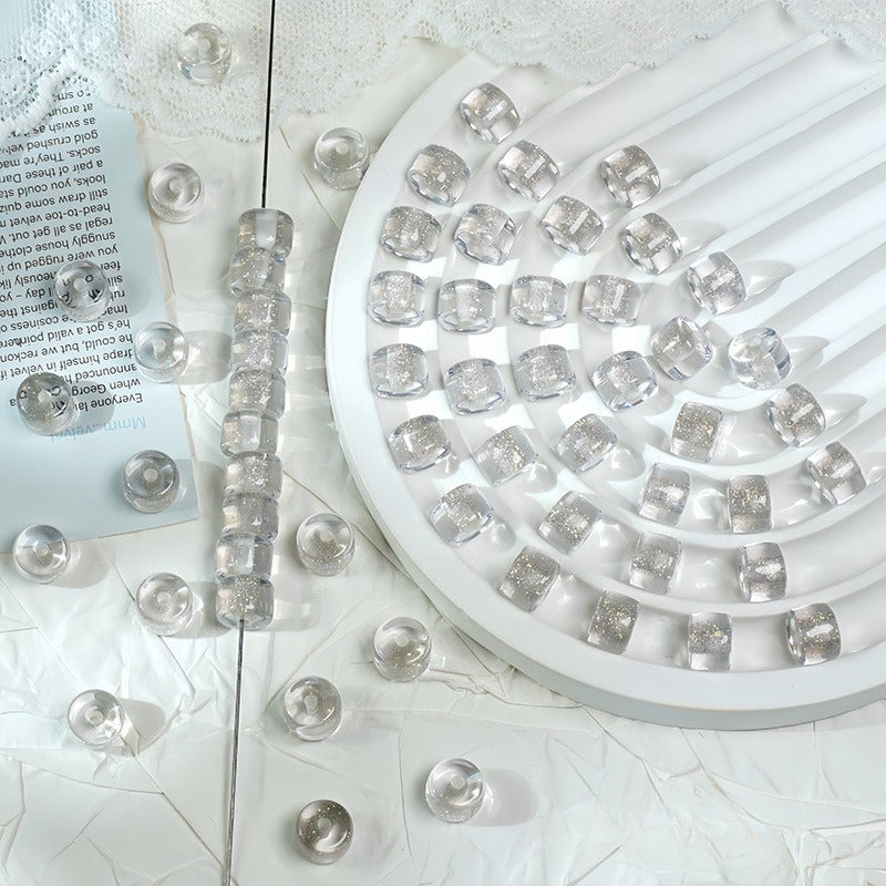 Clear glitter barrel beads strung on a wire and arranged on a white spiral tray with loose beads on fabric