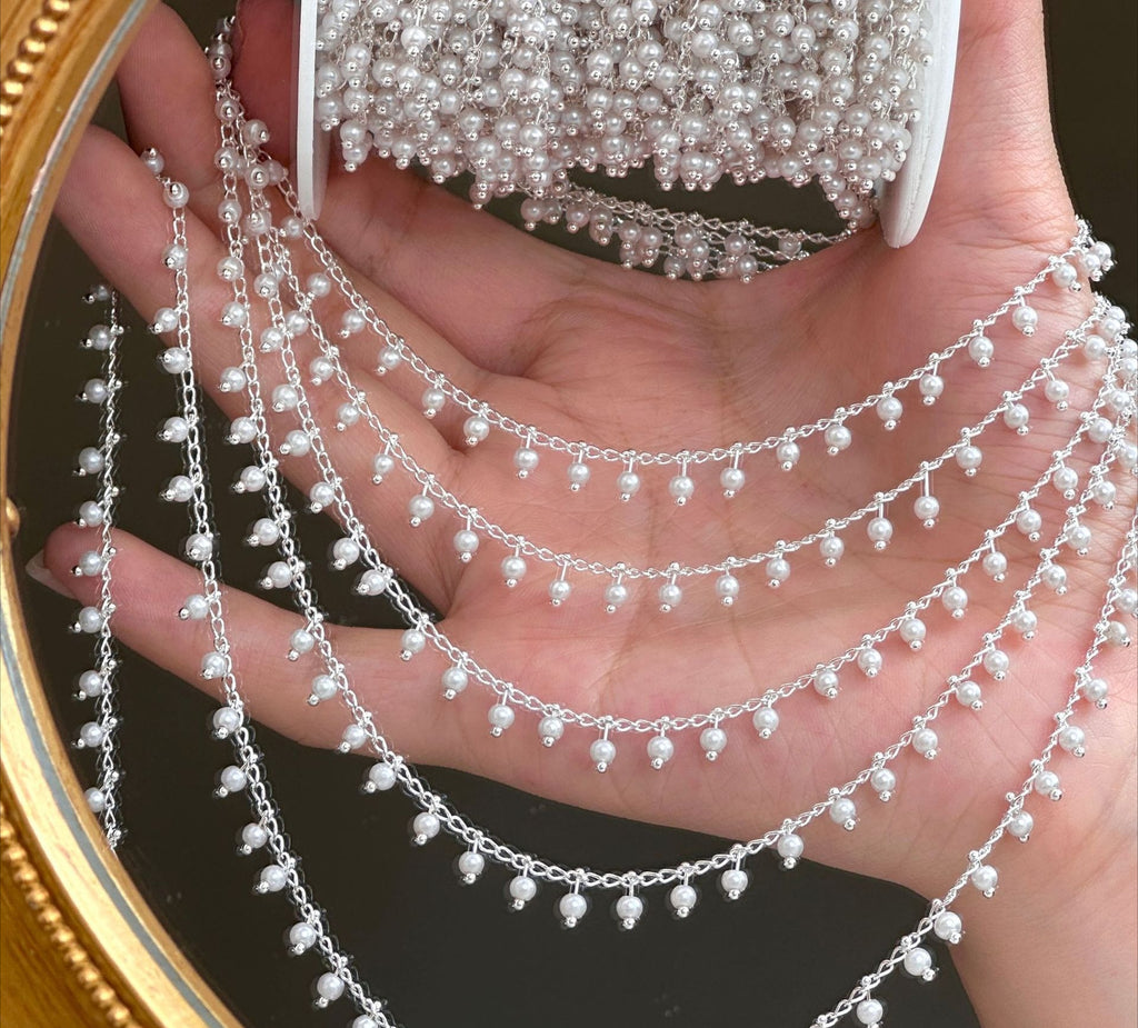 Hand holding silver 3mm white glass pearl fringe chain strands draped across open palm.
