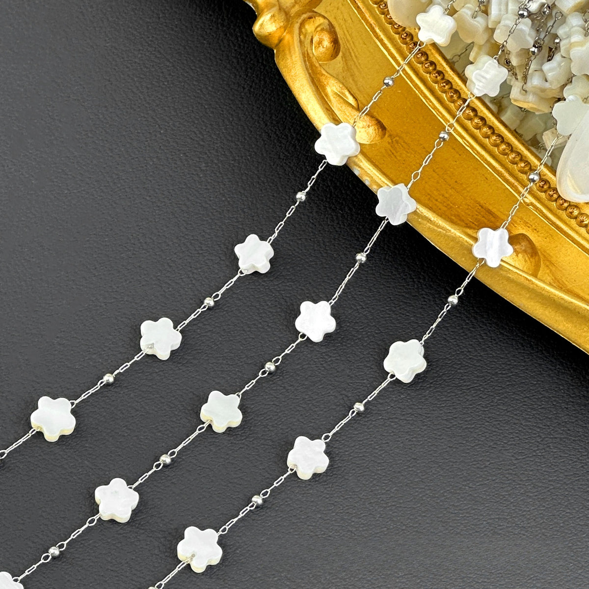 Close-up of silver station chain with white flower-shaped beads and tiny silver beads beside ornate gold tray.