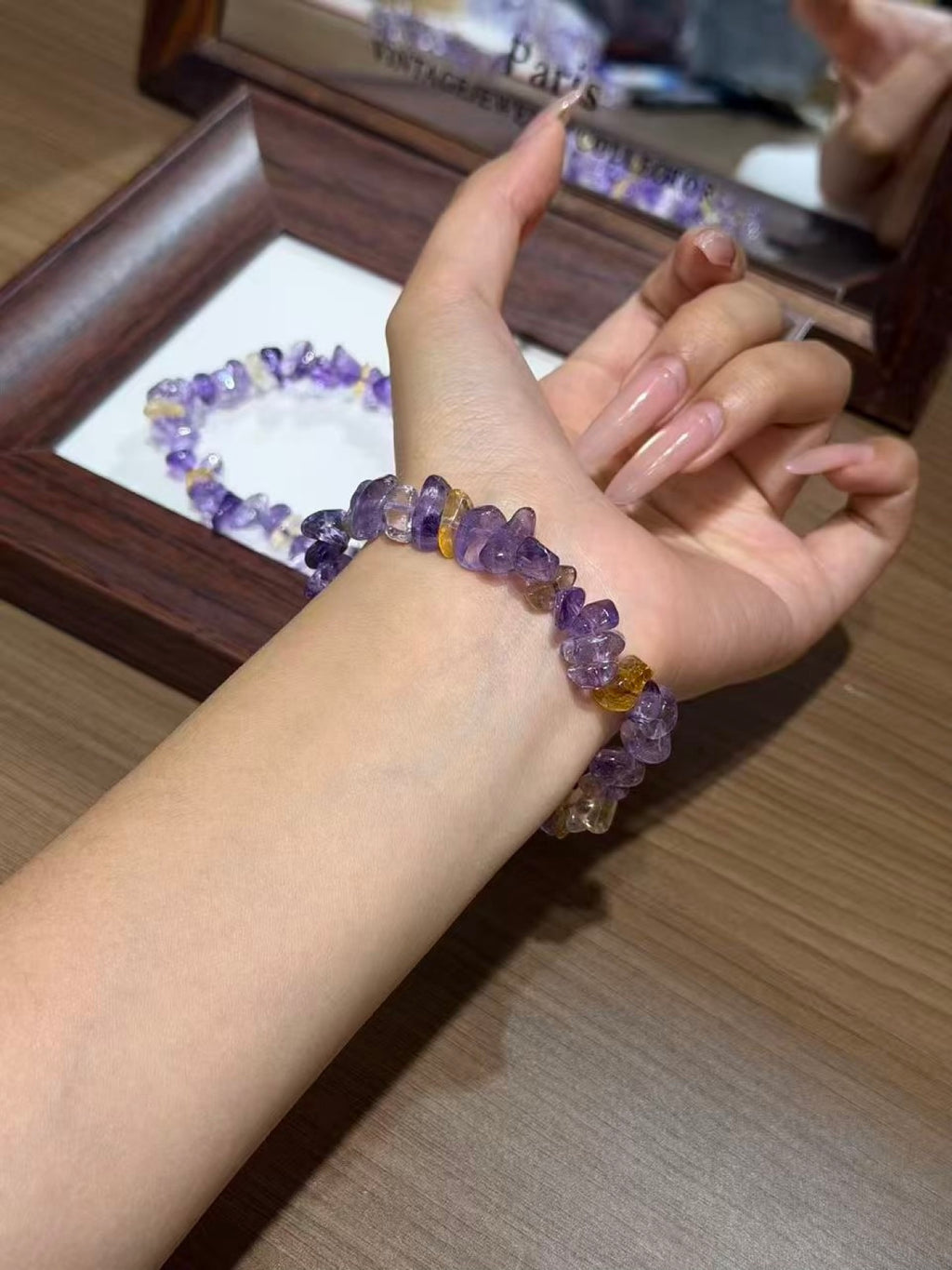 Close-up of an ametrine chip bracelet worn on a wrist, with a matching bracelet resting in a wooden jewelry box in the background