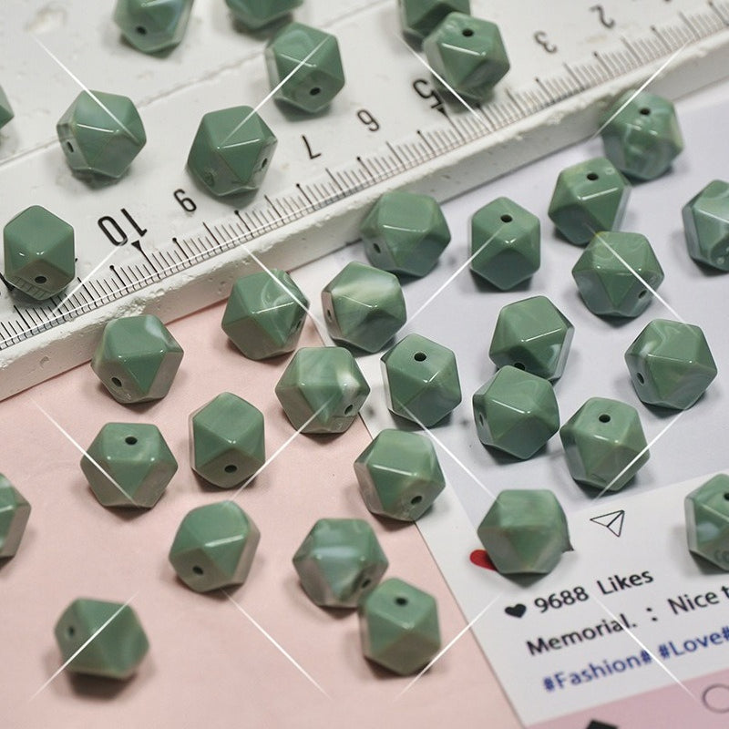 Green faceted geometric beads scattered on a pink and white surface with a ruler
