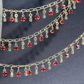 Gold chain with dangling red rhinestones and teardrop charms on dark gray