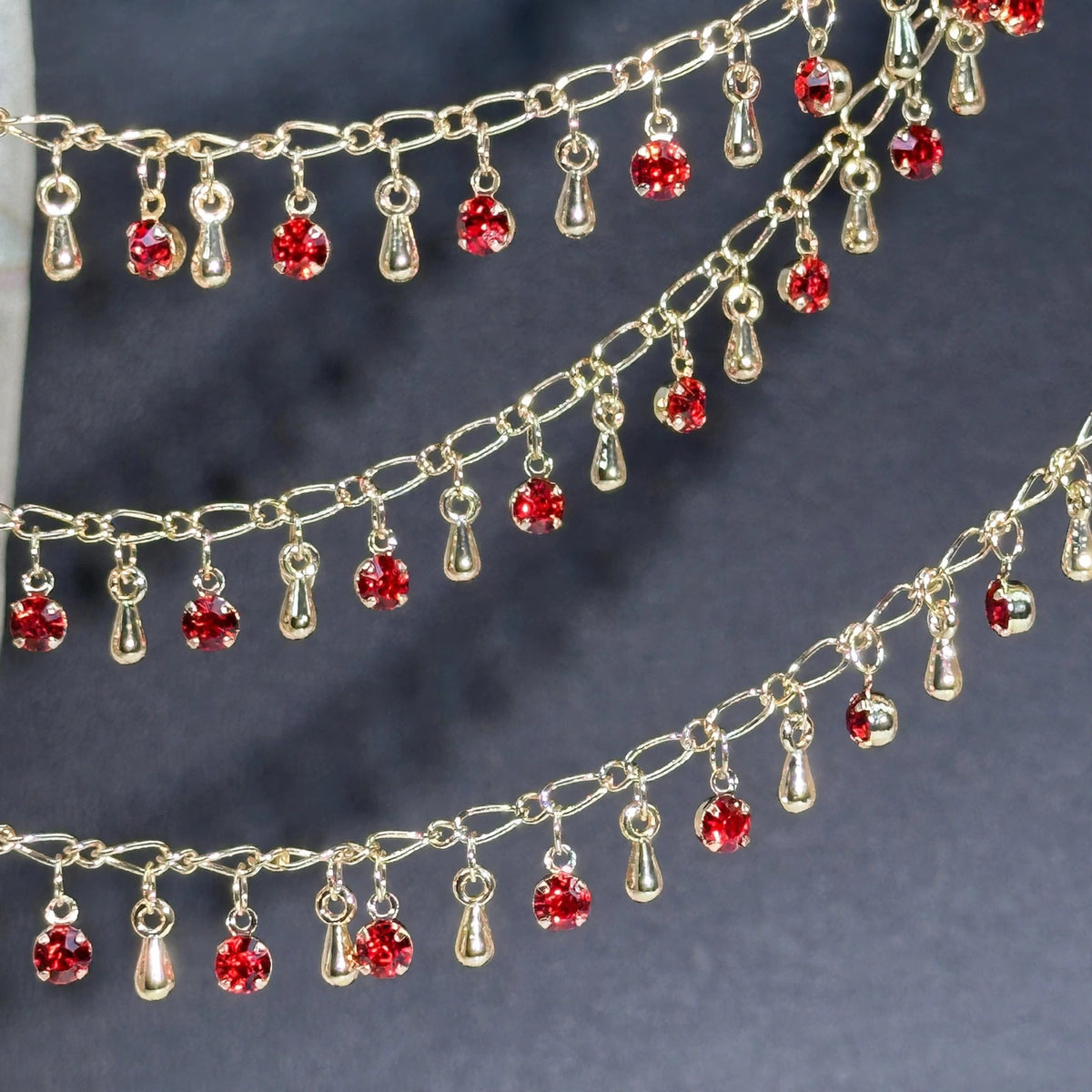 Gold chain with dangling red rhinestones and teardrop charms on dark gray