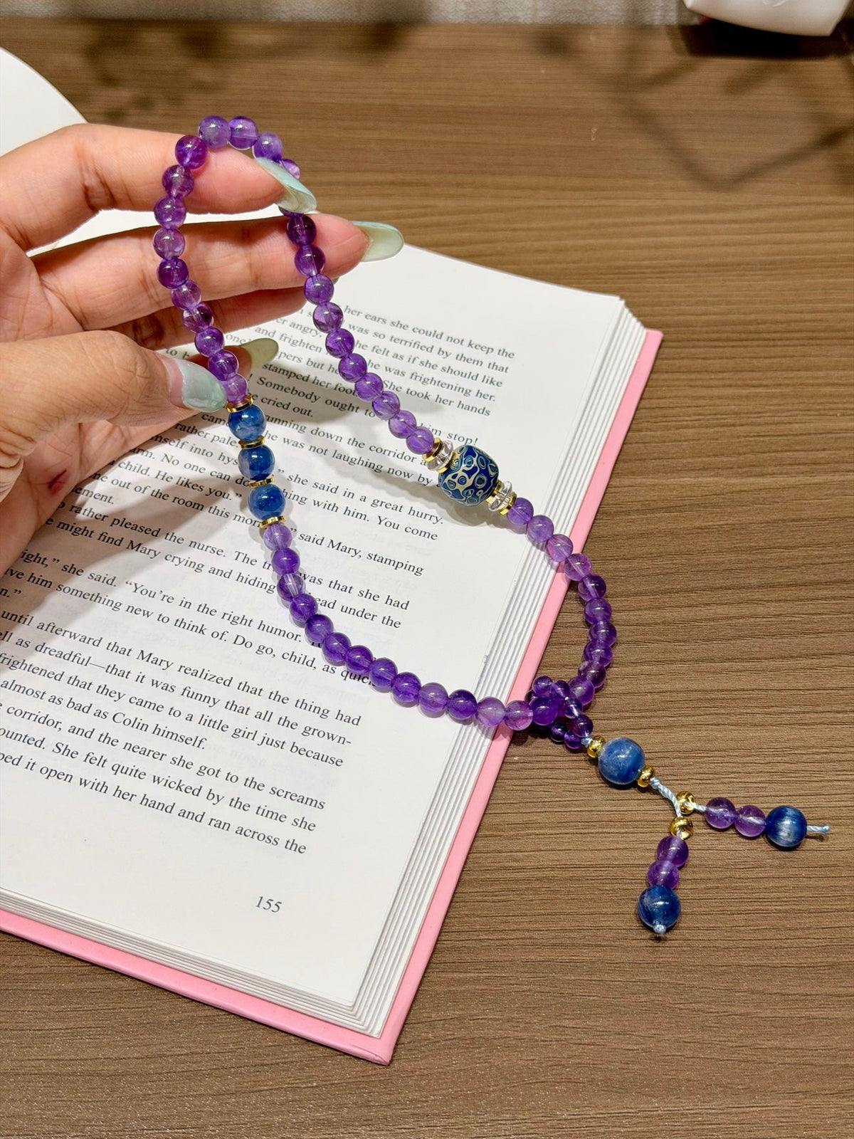 Purple amethyst double-loop bracelet with blue beads held over open book