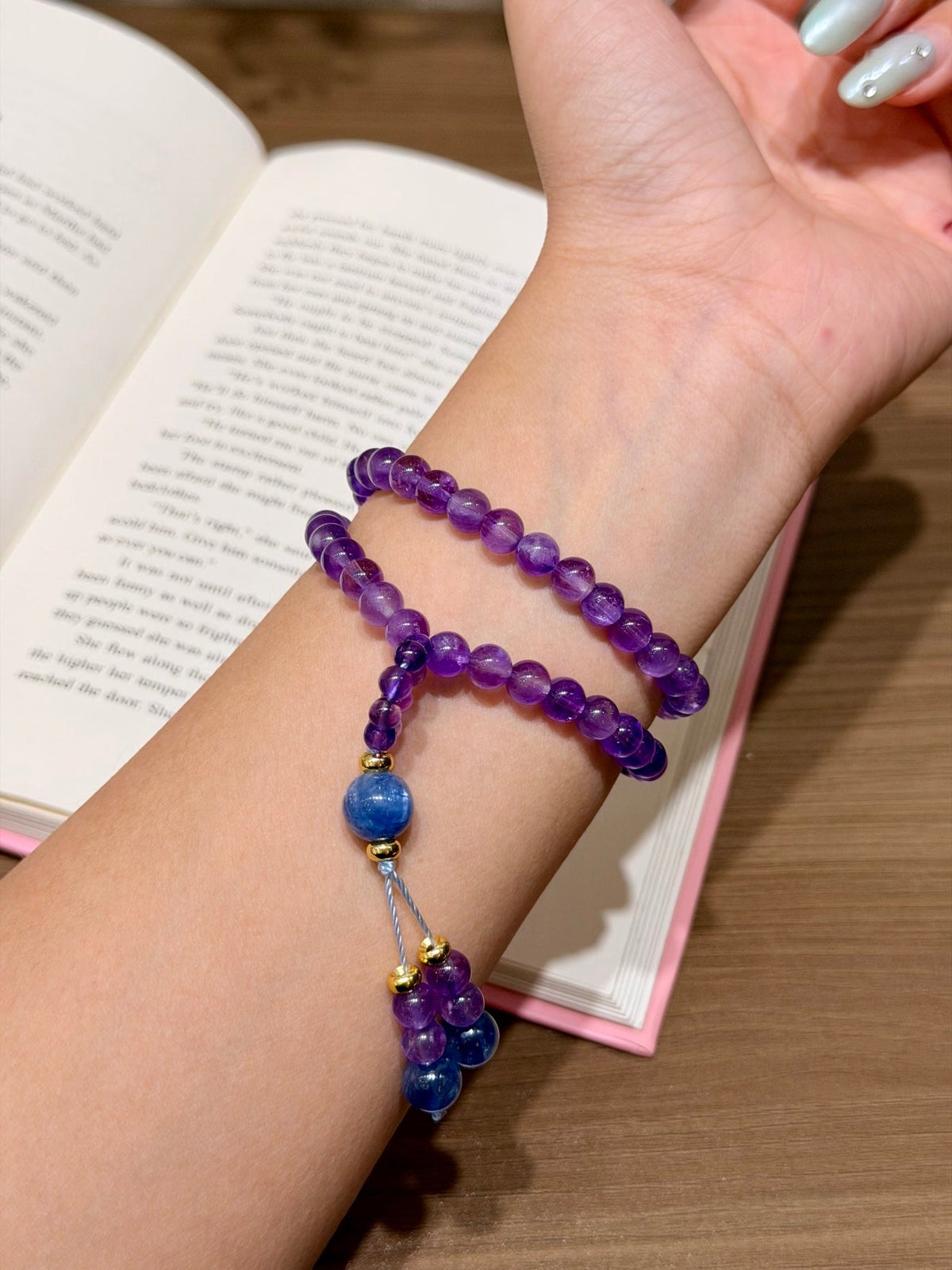 Purple amethyst double-loop bracelet worn on wrist over open book