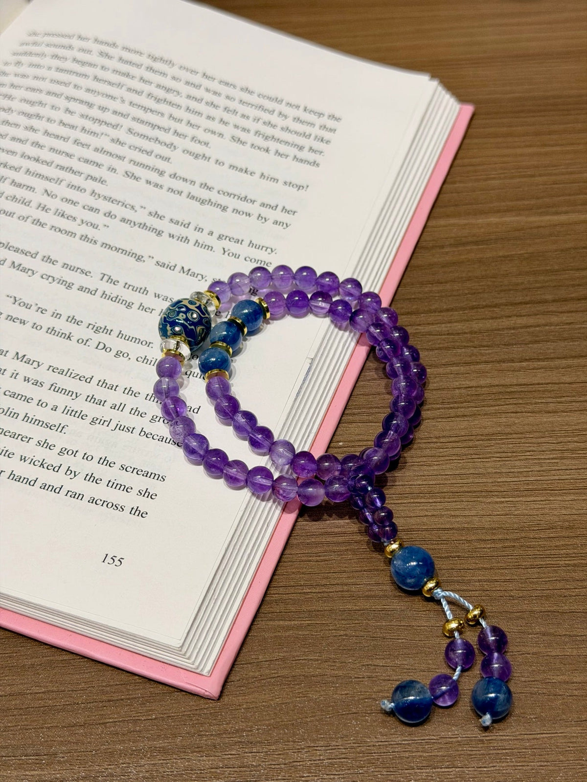 Purple amethyst double-loop bracelet with blue beads draped over open book